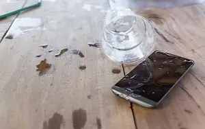 Mobiltelefon auf einem Tisch, das durch Wasser aus einem umgekippten Glas beschädigt wurde