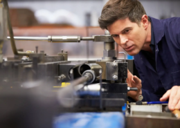 Facharbeiter steht an einer Maschine und prüft ein Werkstück