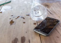 Mobiltelefon auf einem Tisch, das durch Wasser aus einem umgekippten Glas beschädigt wurde