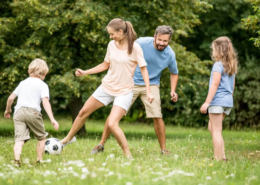 Elternpaar und ihre 2 Kinder spielen im Garten Fußball