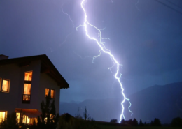 In einem Gewitter ist ein Blitz neben einem Wohnhaus zu sehen