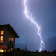 In einem Gewitter ist ein Blitz neben einem Wohnhaus zu sehen
